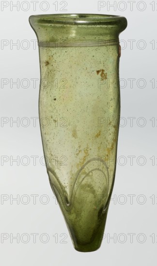 Lamp oil container, deposit provenance, Islamic art, Arabic culture, glass oil lamp, cream enamel thread also at the bottom, 12th–15th century, Syria, or Egypt, Middle East, height 12.0 cm, diameter 5.2 cm, A tall, narrow glass vessel with a rounded flared rim and a tapered pointed base, rendered in translucent green with areas of pale and deeper green tones; the surface shows many small bubbles and a few irregular darker spots and patches, plus a few rusty brown discolorations; there is a subtle applied horizontal ridge near the rim and a decorative wavy applied thread near the lower body creating arched shapes; overall the glass has a slightly uneven, hand-blown texture and a glossy finish.