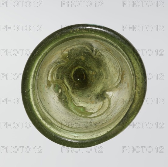 Lamp oil container, Islamic art; Arabic culture; glass oil lamp with cream enamel thread also at the bottom; 12th–15th century; Syria, or Egypt, — Middle East; height 12.0 cm, diameter 5.2 cm., A circular glass object viewed from above with a thick rim and a concave interior, primarily green in color with variations ranging from dark green at the rim to lighter, yellow-green tones toward the center; the glass surface shows swirling, wavy patterns and a few irregular bubbles and speckles, with subtle areas of translucence and cloudy texture, and the background is a pale off-white.