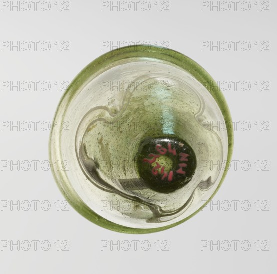 Lamp oil container, deposit provenance, Islamic art, Arabic culture, glass oil lamp with cream enamel thread also at the bottom, 12th–15th century, Syria, or Egypt, Middle East, height 12.0 cm, diameter 5.2 cm, A top-down view of a round glass object with a green rim and a green-tinted interior, showing a few irregular wavy darker lines inside; the glass surface has a cloudy, speckled texture with some areas of lighter and darker green and a small central dark green circular area that contains a few red marks; the background is a smooth light gray.