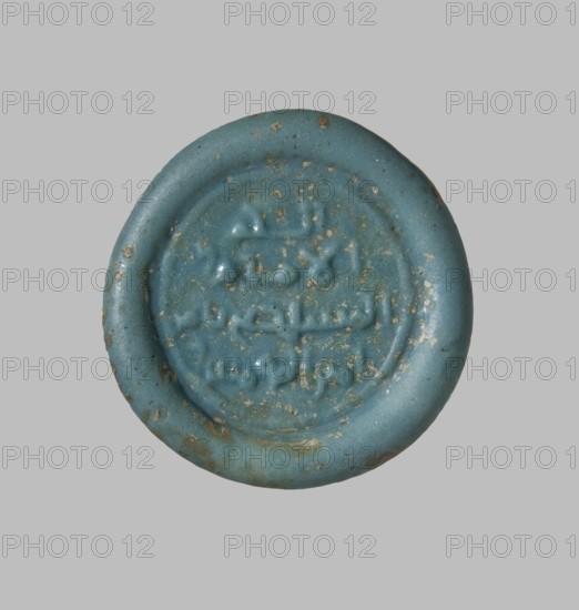 Coin weight with an impression of a seal containing the name of Caliph Al-Mustadi, Islamic art, Arabic culture, Abbasid dynasty 750–1258, inscriptions in Arabic, monetary weight; 1170–1180, Egypt; thickness 0.5 cm, diameter 3.0 cm, weight 8.57 g, A circular object with a raised rim and a recessed central area, shown against a plain gray background; the object is predominantly turquoise blue with small patches of brownish discoloration and speckling across its surface, and it has an uneven, slightly pitted texture with worn areas and shallow raised shapes within the central recess.