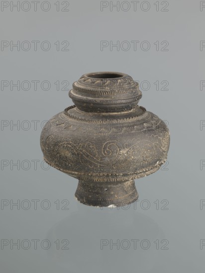 Jug, Islamic art, Persian culture, geometric and geometric-floral ornament, plant twig motif. Jug with a bulging belly on a high foot. Decoration: plant twig and raised geometric patterns. 16th–18th century, Central Asia . Vessel. Height 18.7 cm; width 18.3 cm., A dark grayish-brown rounded vessel with a narrow neck and flared base sits against a pale gray background; the surface of the vessel shows lighter worn patches and speckling and features carved or incised swirling decorative bands and ridged, beaded trim around the neck and shoulder, with a few small chips and rough areas along the rim and base.