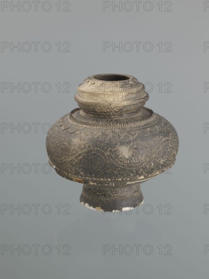 Jug, Persian, Islamic art; 16th–18th century, Central Asia ; ceramic vessel with bulging belly on a high foot; decoration of plant twig and raised geometric and geometric-floral patterns; height 18.7 cm, width 18.3 cm;, A rounded ceramic vessel with a short neck and flared base sits against a plain pale gray background; the vessel is predominantly dark gray to black with areas of lighter gray and beige weathering, and it has carved or incised swirling decorative patterns and bands of raised ridges around the neck and shoulder, with small spots of white chips and worn edges along the base.