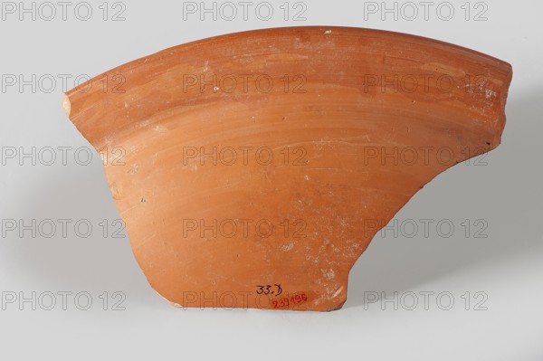 Fragment of a terra sigillata plate. Fragment of the rim of a deep plate with a flat, wide rim and a frieze with predatory animals. On the preserved fragment, facing right: a lioness on the right, with short fur marked with circles and a panther with longer fur jumping. Orange clay, red glaze. The dimensions of the entire plate can be reconstructed as approx. 43.9 cm in diameter, 7.6 cm in height. Late 3rd–4th century, Tunisia. Plate; fragment width 13.4 cm, length 22.1 cm., A fragment of a curved terracotta object with a smooth surface in shades of orange and reddish-orange, showing areas of lighter orange wear and small patches of white residue; the edges are irregular and chipped with some exposed lighter clay, and the piece rests against a pale gray background with soft shadows.