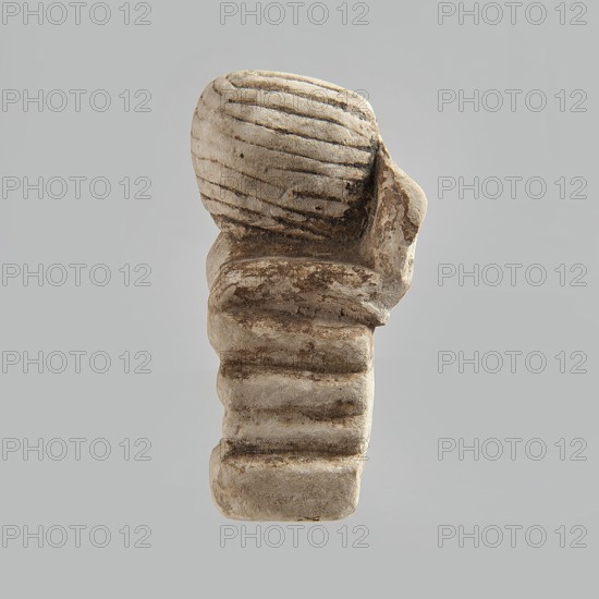Head of a polychrome figurine, which originally probably depicted a woman lying on a bed with her head propped up on a pillow. The woman's head is shown wearing a short, striped wig. Behind the head, a woman's hand is visible, which, like the head, rests on an object that may represent a pillow or bolts of cloth. Fragment of a figurine. 332 BC–395 AD; Ptolemaic Period–Roman Period. Egypt. Figurine. Height 2.8 cm, width 5.6 cm, depth 2.5 cm., A weathered stone object with a rounded top featuring carved horizontal grooves, sitting on a stacked, ribbed base; the surface shows areas of rough texture and erosion with darker patches. The visible colors are shades of beige, light gray, and darker brown on a pale gray background.