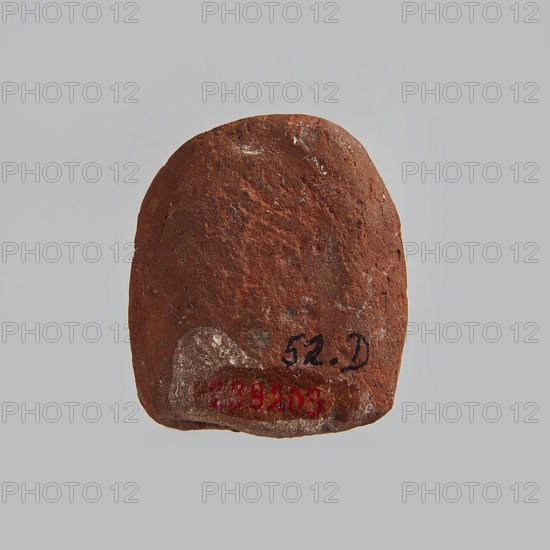 Mold for pressing a figurine of Ptah the dwarf probably made by pressing from a stone matrix. The head wears a flat cap, a wide face with long, thin mustaches or swallowed snakes; in the hands two oval objects feathers?. Legs are curled up. The upper torso is covered by a beaded necklace; otherwise the figure is naked. Technological grooves on both sides of the figurine. Small incisions above the head. The form is semi-oval, rounded at the bottom. Ptah the dwarf mythology, snakes, feathers iconography. 664–332 BC; Late Period, Egypt. Form. Height 2 cm, width 4.2 cm, depth 4.7 cm., A roughly rounded, flat object with a coarse, uneven surface in shades of brown and reddish-brown, with small patches of lighter tan and gray; the object sits against a light gray background and shows a few smudges of dark black and faded red on its lower area.
