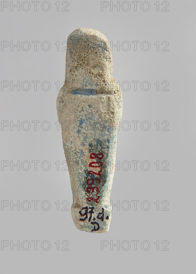 Ushabti. Carelessly made figurine with schematic facial features, in a narrow wig revealing the ears, with a rather short beard. In his hands he holds a mattock. The back is flat; the end of the wig is marked with an engraved line. Feet on a pedestal. Glaze almost completely worn away. Third Intermediate Period, Egypt. Ushabti; height 6.5 cm, width 2.1 cm, depth 1.3 cm., A weathered small figurine with a rounded head and tapered body, showing a rough, pitted surface texture and traces of worn pigment; the object displays colors including beige, sandy tan, muted blue, and small areas of red and dark markings; the background is a uniform light gray.
