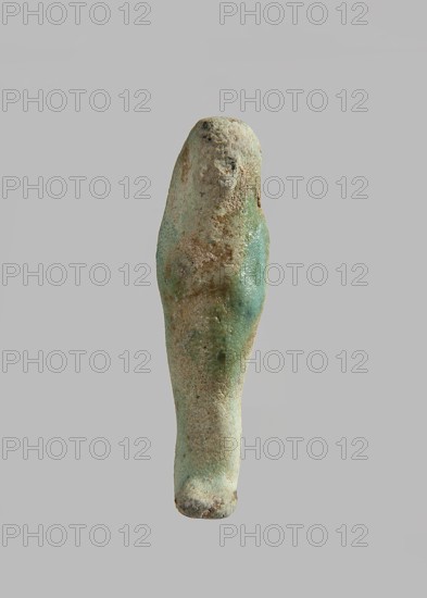 Ushabti, Mass-produced ushabti figurine with very schematic shapes, with a barely marked face and crossed arms. Flat back. Glaze partially discolored. Third Intermediate Period, Egypt. Ushabti; height 5.8 cm, width 1.7 cm, depth 1 cm., A small elongated object resembling a human figure with a rounded head and tapered body, shown against a plain light gray background; the surface appears worn and textured with a mix of colors including pale green, turquoise, sandy beige, and touches of darker brown, with areas that look rough and pitted and other smoother, slightly glossy patches.
