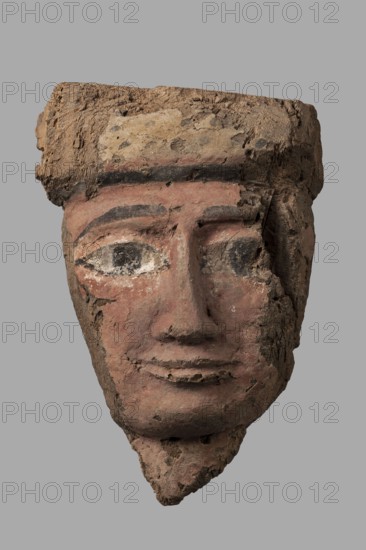 Sarcophagus mask with a partially preserved fragment of a wig above the forehead painted yellow with traces of black polychrome. Separated from the forehead by cherry-red and black bands. The eyes are relatively large with black rims, pupils, and eyebrows; the whites are white. The nose is long, narrow, widening evenly towards the nostrils. The mouth is primitively modeled. A fragment of the neck is preserved under the chin. The face is painted cherry-red. Partially preserved mounting pegs at the back. Ptolemaic Period, 332–30 BC; Egypt. Sarcophagus mask; height 25.7 cm, width 18 cm, thickness 8.2 cm., A weathered sculpted face with a textured headdress rendered in shades of brown, tan, pinkish-red, black, white, and grey; the face shows a smooth worn surface with visible cracks and chipped areas, large painted eyes with dark pupils and white surrounds, dark painted eyebrows and a horizontal dark band across the forehead, a defined nose and slightly smiling lips with worn edges, and a ...