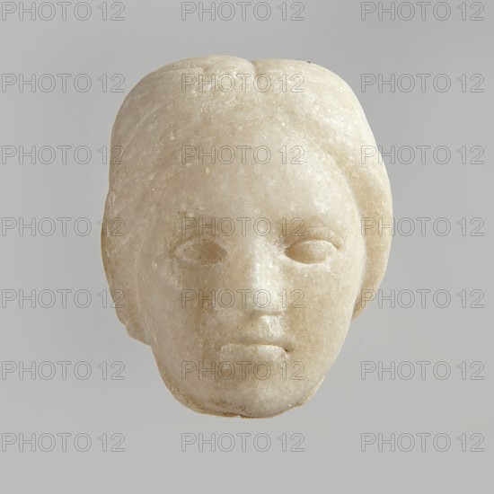 Fragment of a female figurine. Fragment of a small-sized sculpture or sculptural group. The depiction has portrait features. The face is oval, the nose is large, the mouth is closed in a slight grimace. 2nd–3rd century AD, Egypt. Terracotta figurine, sculpture; height 8.5 cm, width 4.5 cm, depth 5.5 cm., A pale stone sculpted head with smooth rounded contours and a neutral expression is centered against a light gray background; the surface shows subtle variations of off-white, cream, and beige with faint textured speckles, shallow eye sockets and simplified facial features, a defined nose and lips, and hair indicated by gentle grooves framing the sides and top.