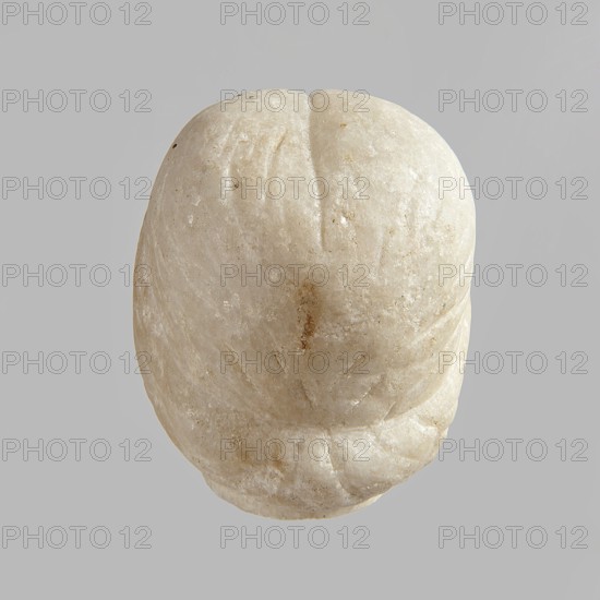 Fragment of a female figurine. Fragment of a small-sized sculpture or sculptural group with portrait features. The face is oval, the nose is large, the mouth is closed in a slight grimace. 2nd–3rd century AD, Egypt. Figurine, sculpture; height 8.5 cm, width 4.5 cm, depth 5.5 cm., A rounded stone object in off-white and beige tones sits against a flat gray background, showing a smooth, slightly translucent surface with small rough patches and areas of darker beige discoloration; the object has a central shallow groove and several faint curved indentations, with a lower edge that appears slightly chipped and irregular.