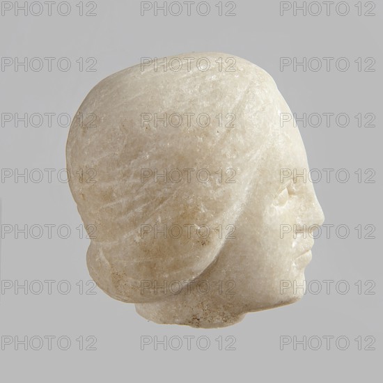 Fragment of a female figurine. Fragment of a small-sized sculpture or sculptural group with portrait features. Oval face, large nose, mouth closed in a slight grimace. 2nd–3rd century AD, Egypt. Terracotta figurine sculpture. Height 8.5 cm, width 4.5 cm, depth 5.5 cm., A carved stone head viewed in profile against a plain light gray background, showing a smooth, rounded top and stylized hair rendered with subtle grooves; the facial features include a pronounced forehead, a defined nose, gently closed lips, and a softly rounded chin. The surface of the stone displays a pale off-white to creamy beige coloration with variations of light tan and faint speckles, and areas of slight translucency and natural grain. The overall texture appears polished in places and slightly rough in others, with soft shadows accentuating the form.