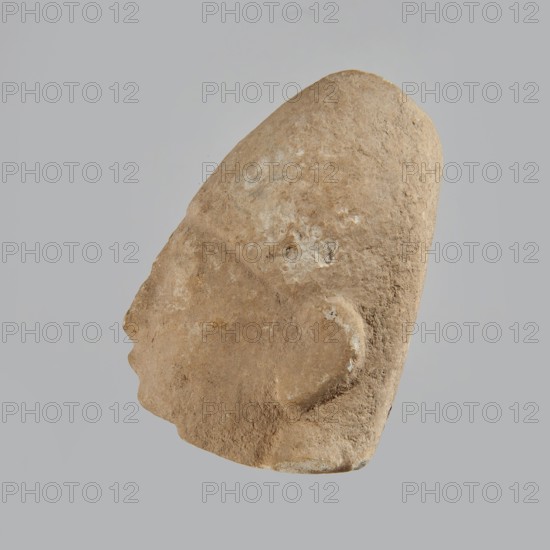 Head of a man, Archaic Period, Cyprus; figurine; height 7 cm, width 5 cm, depth 5.5 cm., A roughly triangular, weathered stone sculpture of a human head shown in profile against a plain light gray background, with a textured surface in shades of beige, tan, and light brown and areas of lighter whitish discoloration; the profile shows a pronounced forehead and sloping nose, an outlined ear, and a rounded chin, with natural pits and roughness visible across the form.