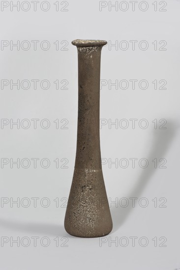 Bottle; maker, 1st century BC–1st century AD; Egypt; vessel., A tall, narrow ceramic vessel with a flared rim and a rounded, tapered base stands against a light gray background, showing a textured surface with speckled areas; the object is primarily brown with lighter beige and off-white speckles and darker brown spots, and it casts a soft shadow to the right on the pale background.