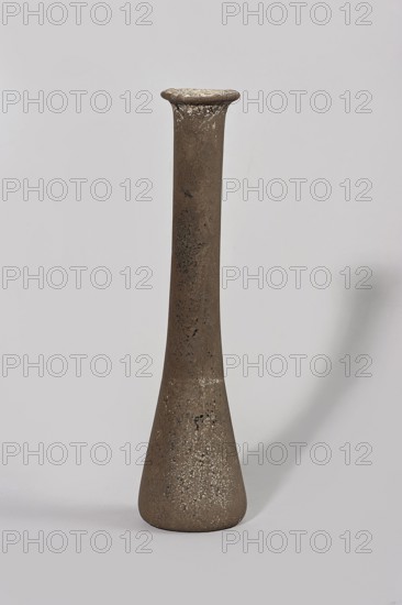 Bottle; maker, gift; 1st century BC–1st century; Egypt; vessel, A tall, narrow vase with a flared rim and a rounded, tapered base stands against a pale gray background, showing a rough, textured surface in shades of brown with patches of darker brown and areas of lighter, almost white speckling; the vase casts a soft shadow to the right.