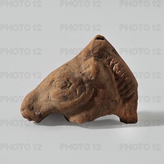 Horse head, Fragment of a terracotta figurine showing a horse's head with a mane. Hellenistic or Roman period, 323 BC–476 AD; Egypt. Figurine animals; horse iconography. Height 5.4 cm, width 3.1 cm, depth 6.7 cm., A small sculpted object shaped like an animal head, shown against a pale gray background, with the object in shades of brown and reddish-brown; the head has a pronounced snout, carved eye area, and a textured mane or ridged area along one side, with visible surface irregularities and rough, weathered texture.