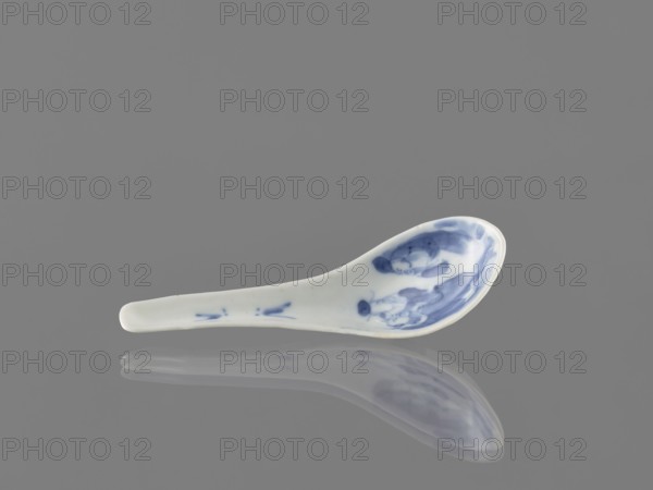 Spoon, ceramic, blue-and-white porcelain, figurative scenes with bats iconography, cutlery, Chinese, Qing dynasty 1644–1911, 18th century, Harbin China, length 12.5 cm., A white ceramic spoon with blue painted decorative marks on its bowl and a few blue accents on the handle rests on a smooth gray surface, casting a soft reflective shadow; visible colors include white, blue, gray, and subtle off-white tones.