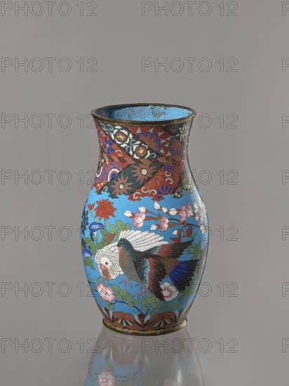 Vase, doves, flowers iconography, Japanese art, Japanese culture, birds, Meiji 1868–1912, peonies, chrysanthemums, wolfberries, kachôga iconography, sakura iconography, cloisonné enamel. Belly flowing smoothly into a short, thick, slightly parted neck. Cloisonné enamel on copper; brass foot and spout frame. Ca. 1870–1880 Meiji Period, 1868–1912. Japan, Nagoya. Vessel; height 26.5 cm, width 12.6 cm., A vase with a glossy sky-blue background decorated with floral and bird motifs; the vase shows a group of flowers in red, pink, white, blue, and green leaves, and two birds with white, brown, black, and blue feathers; the neck area has a patterned band in red, black, blue, white, and gold tones, and the rim and base have metallic gold accents; the interior of the vase appears turquoise-blue with darker spots, and the vase is reflected on a neutral gray surface and set against a plain gray backdrop.