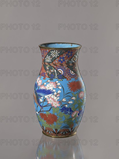 Vase, Revindication Kraków. Doves, flowers; Japanese art; Japanese culture; Choynowski, Józef 1833–ca.1915. Birds. Meiji 1868–1912. Lilies, cloisonné enamel, chrysanthemums, wolfberries, sakura, butterflies, dragonflies, kachôga. Vase with a thick neck, parted towards the spout. Cloisonné enamel on copper. The spout and foot are enclosed by brass rings. Ca. 1870–1880 Meiji Period, 1868–1912. Japan, Nagoya. Vessel. Height 26.5 cm; width 15.5 cm., A small decorative vase with a flared rim and rounded body sits against a neutral gray background; its surface is predominantly bright blue with a detailed floral and bird design in colors including red, pink, white, green, dark blue, black, and gold tones, featuring blossoms, leaves, and a bird with blue and brown plumage amid leafy stems, and a patterned band of darker colors and floral motifs near the top, with a thin metallic rim and a reflective base showing a faint mirrored image.
