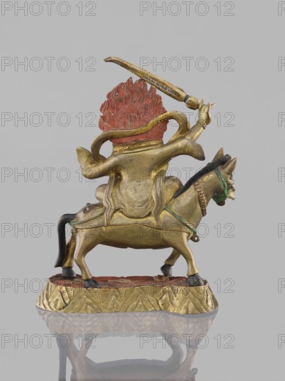 Palden Lhamo;, Tibetan Buddhist sculpture; 19th century; materials unspecified; depiction features a dharmapala wrathful protector with mules and skulls; possible origin China or Mongolia; height 14.8 cm, width 13.0 cm., A small sculpted figure of a mounted animal with a humanlike rider shown from the back, the rider with a textured flamelike form behind its head painted red and a metallic gold body, the rider holding a curved object above its head in a raised arm, the mount rendered in metallic gold with darker hooves and a dark tail, green accents on the mount's bridle and harness, the figure positioned on a patterned gilded base with a red surface, all set against a plain light gray background.