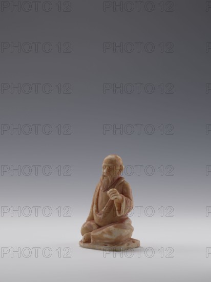 Sage, unknown sculptor; figurine of a bonza priest; Chinese, Qing dynasty 1644–1911, 19th century; material: sculpture; dimensions: height 10.4 cm, width 6.9 cm, depth 5.0 cm. Maker/persons associated: Choynowski, Józef 1833–c.1915; Dawidow, Alexander Petrovich 1838–1885., A small carved figurine of a seated elderly man with a long beard, wearing flowing robes and sitting on a flat base; the figure is carved from a stone with warm beige, tan, and light brown tones with subtle creamy white patches, and the background is a smooth gradient of gray ranging from darker gray at the top to lighter gray near the bottom.