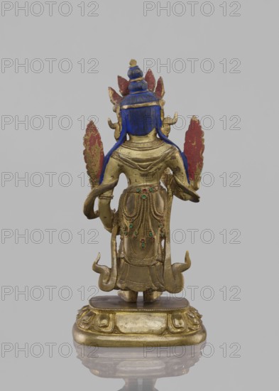 Maitreya Buddha of the Future, Tibetan Buddhist art, figurine, bodhisattva iconographic, lotus throne iconographic, Buddhist art, buddha iconographic, Buddha of the Future, 19th century, Southern China, Tibet, sculpture, height 16.8 cm, width 7.6 cm, The image shows the back of a small gilded statue standing on an ornate rounded base; the statue has a blue headdress and blue sections along the shoulders, a few red leaf-like ornaments behind the head, and small green round insets on the decorative drapery at the back; the metal surface is predominantly gold with areas of wear revealing darker tones, and the background is a uniform light gray.
