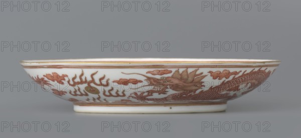 Plate, deposit, Chinese, Qing dynasty 1644–1911, Guangxu period 1875–1908. Porcelain dish, height 3.2 cm, diameter 16.7 cm. Decorated in the mirror and on the outer wall with a pair of dragons with a pearl among clouds on a white background. Signed., A shallow round dish with a low foot, shown in profile against a gray background, made of white ceramic with decorative reddish-brown painted motifs including a stylized dragon and swirling cloudlike shapes, with thin golden bands along the rim and near the base, and subtle shading on the dragon's scales and features.