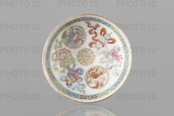 Bowl, Chinese colored porcelain saucer-vessel with floral decorations and meander ornament; Qing dynasty, Guangxu period 1875–1908, 2nd half of the 19th century; related to Boxer Rebellion 1899–1901; height 2.7 cm, diameter 7.5 cm., A small circular porcelain dish with a white interior and a gilded rim, decorated inside with a group of round medallion motifs and flowing ribbon-like shapes in colors including pale green, pink, orange, blue, purple, and gold, and a patterned border around the inner edge in alternating turquoise, green, and pink with gold highlights; the background surrounding the dish is a uniform gray.