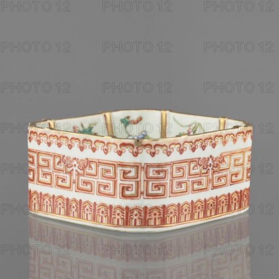 Vessel, Chinese, Qing dynasty Daoguang, 1821–1850. Ceramic colored porcelain vessel decorated on the outside with floral decorations, lambrequin pattern and meander strip. Height 6.0 cm; width 12.8 cm., A shallow hexagonal ceramic dish with an off-white base color decorated with intricate red and gold geometric and floral patterns around its exterior, a scalloped red and gold border near the top edge, and a band of red architectural-style motifs along the bottom; the interior shows hints of painted floral motifs in green, pink, and blue; the rim has small areas of wear revealing darker spots, and the dish sits on a reflective gray surface with a gray background.