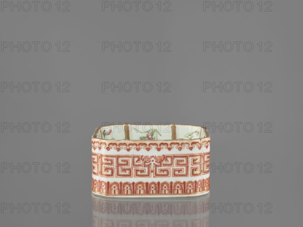Vessel, Chinese, Qing dynasty Daoguang period, 1821–1850. Porcelain, polychrome enamel decoration; decorated on the outside with lambrequin ornament and meander strip and floral decorations. Height 6.0 cm; width 12.8 cm., A small rectangular ceramic container with scalloped top edges sits centered against a plain gray background, showing a glossy surface and faint reflection below. The exterior of the container features a repeating geometric band and ornamental borders in reddish-orange and gold tones on a white base, while the interior displays painted floral motifs with green and pink accents and touches of gold along the rim. The visible colors include gray, white, reddish-orange, green, pink, and gold.