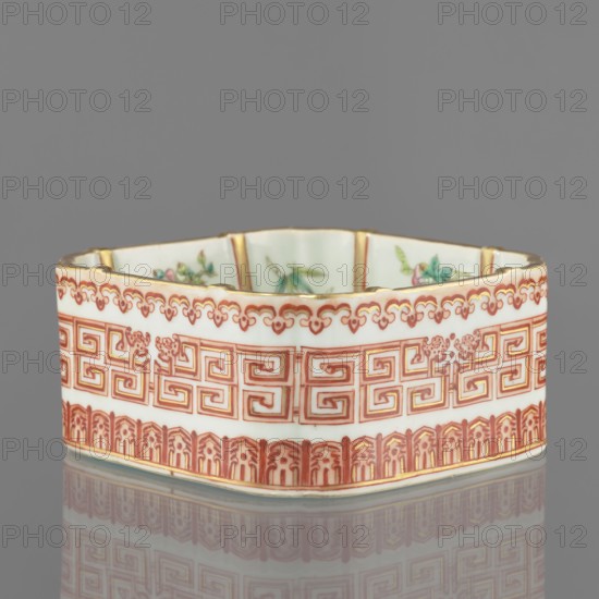Vessel, Chinese, Qing dynasty, Daoguang period 1821–1850; ceramics, colored porcelain; decorated on the outside with lambrequin ornament and meander strip; floral decorations; vessel; height 6.0 cm, width 12.8 cm., A hexagonal ceramic dish with a white base color and decorative patterns in red and gold around its exterior, showing a band of geometric motifs above a border of stylized arches, with a scalloped red-and-gold trim along the top edge; the interior rim shows painted floral elements in green and pink, and the piece sits on a reflective gray surface that mirrors its colors.