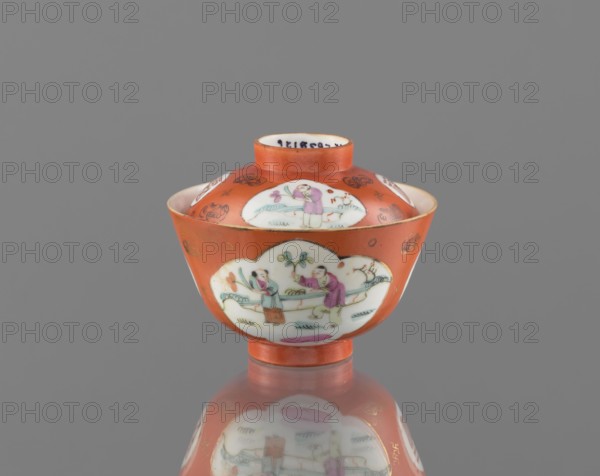 Bowl with a lid, ceramics; colored porcelain; Chinese, Qing dynasty Tongzhi period, 1862–1874; subject: bats and swastikas loosely placed in the background of the decoration, genre scenes; inscriptions: hieroglyphs; function: vessel; height 8.6 cm, diameter 10.3 cm., A small round bowl with a lid sits on a reflective surface against a gray background; the bowl is predominantly orange with white cartouche-shaped panels showing painted scenes of people wearing clothing in colors like pink, purple, green, and light blue, and there are small decorative motifs in gold on the orange areas; the rim and base show thin gold accents, and the reflection of the bowl and its painted panels appears on the surface below.