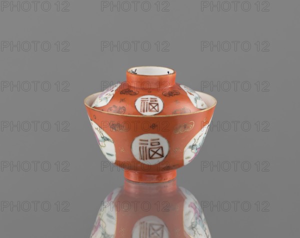 Bowl with a lid, ceramics, colored porcelain, Qing dynasty Tongzhi period, 1862–1874, China; vessel with bats and swastikas loosely placed in the background of the decoration; genre scenes; hieroglyphs; height 8.6 cm, diameter 10.3 cm., A small lidded bowl with a rounded body and a short pedestal, predominantly orange with a glossy finish, decorated with several white circular medallions containing geometric line patterns and stylized motifs, and a few painted figural scenes in pastel colors including pink, green, and light blue. The rim and foot edges show thin gold accents. There are small gold cloud-like motifs and tiny decorative marks scattered on the orange surface. The interior visible at the top is white with a narrow orange band near the rim. The object sits on a reflective gray surface that mirrors the colors and shapes, and the background is a smooth medium gray.