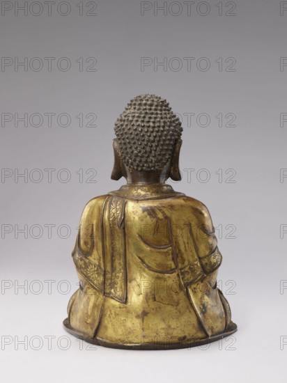 Buddha, militia deposit, Chinese art, Chinese culture, Qing 1644–1911, Qing style, sculpture, casting, Chinese Buddhism, Buddhist art, ushnisha, 19th century, China, figurine; height 32.0 cm, width 23.5 cm, weight 6.255 kg, The image shows the back view of a seated statue with a textured head and elongated ears, wearing a draped robe with decorative borders; the statue appears metallic with predominant gold and darker brown tones, set against a neutral gray background that transitions to a lighter gray toward the bottom.