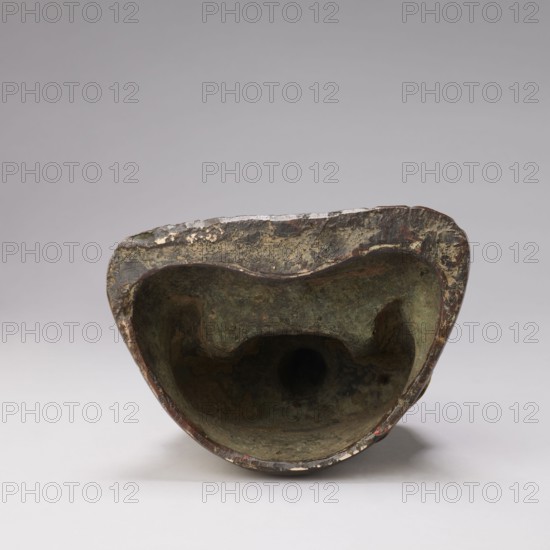 Buddha; unknown creator; cast bronze figurine; Chinese; Qing dynasty 1644–1911, 19th century; Buddhist art depicting Ushnisha; sculpture; height 32.0 cm, width 23.5 cm, weight 6.255 kg; militia deposit, An irregularly shaped hollow object with a rough, textured surface shown from the open end, displaying a weathered interior in shades of green and brown and an outer rim with patches of darker brown and metallic-looking wear; the background is a smooth gradient of light gray and the foreground surface is a pale gray, with small areas of off-white and hints of reddish discoloration along the edge.