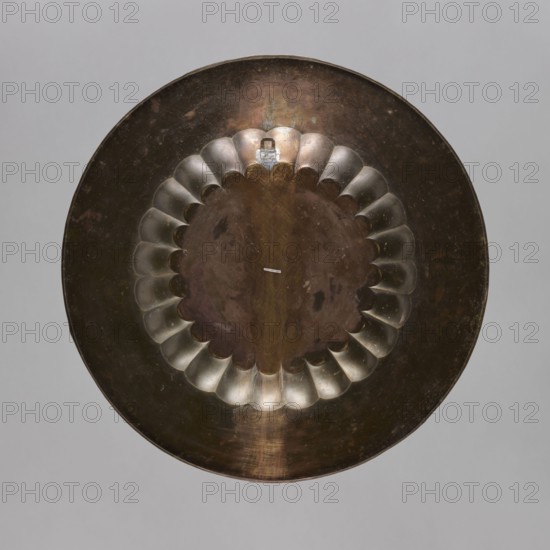 Tray, brass tray with separate facet; engraved and painted decoration depicting a central rosette and floral ornaments placed around it, including flowers, leaves, plant and geometric ornaments; 19th–20th century, India; vessel; height 2.0 cm, diameter 59.0 cm., A round metallic object with a scalloped inner ring centered within a wider rim, showing a mix of brown, bronze, copper, silver, gray, and hints of dark green tones, with a few areas of lighter metallic sheen and some darker blemishes on the surface.