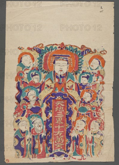 Votive plaque and surrounding deities, nianhua New Year's picture, Chinese, early 20th century, Hebei, graphic print, height 48.5 cm, width 33.0 cm, A colorful painted scene on aged paper showing a central seated figure with a large ornate headdress and a serious facial expression, surrounded by a group of smaller figures with varied headgear and robes; the composition includes decorative floral and scroll-like motifs around the central figure and a vertical decorative panel beneath them. The visible colors include red, orange, teal, turquoise, purple, blue, beige, and touches of green and black. The background paper is off-white with a gray border visible around the sheet, and there are visible creases and small tears along the edges.