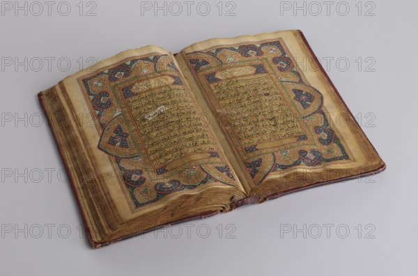 Quranic manuscript, unknown calligrapher, Islamic art, Ottoman dynasty 1299–1922, Arabic manuscript, manuscript written in Naskh script; illuminated, contains two pages for Surah XVII and sixteen later leaves. Paper: striated, smoothed, cream, saffron-colored. 18th century, 19th century additions. Central Asia, Khiva. Manuscript; height 23.0 cm, width 14.5 cm, thickness 4.2 cm., An open ornate book rests on a pale gray surface, showing two aged pages with decorative borders and illuminated patterns; the paper is yellowed and browned at the edges, with visible wear and slight warping. The decoration features intricate motifs in gold tones, deep blue, red, green, and touches of white, forming symmetrical panels and corner embellishments around the central text areas. The binding and fore edge show worn brown leather and darker brown staining, and the gutter has creases where the pages meet. Overall the scene includes colors such as beige, brown, gold, blue, red, green, white, and pale gr...