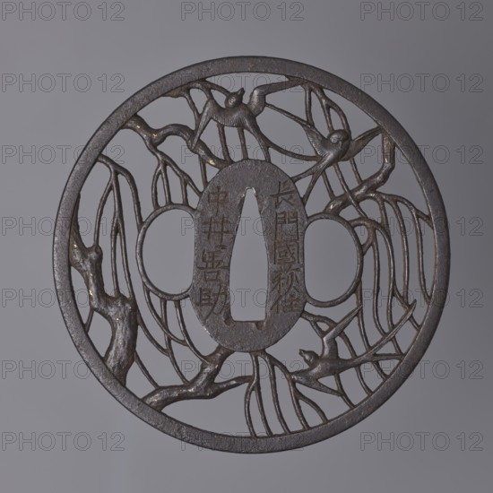 Crossguard tsuba, Nakai Tomotsune II; Nakai school. Decorated with openwork positive openwork depicting swallows among willow branches. Small gold spots nunome technique on the branches. Rectangular edge kaku mimi. Signed. Early 18th century Edo period, 1603–1868. Japan, Nagato province, Hagi. Tsuba; diameter 8.3 cm; thickness 0.4 cm., A circular metal object with an openwork design showing a group of stylized birds perched among winding, branch-like forms; the metal has a dark brown to black patina with small areas of lighter brown and subtle golden flecks, and the background is a smooth mid-gray.