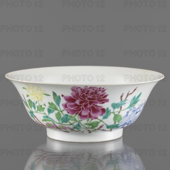 Bowl, porcelain, semicircular body widening toward the upper edge; white, transparent, fritted glaze with overglaze enamel-painted decoration of rocks and peonies in colored porcelain; Qing dynasty, Yongzheng period 1723–1735, China; height 7.6 cm, diameter 19.5 cm, weight 0.3 kg., A shallow white porcelain bowl with a flared rim sits against a gray background, decorated around its exterior with painted floral motifs including a large deep magenta flower, a pale yellow blossom, and a smaller blue flower, connected by green leaves and brown stems; the bowl rests on a short foot and casts a subtle reflection on the surface below, and the visible colors include white, gray, magenta, yellow, blue, green, and brown.
