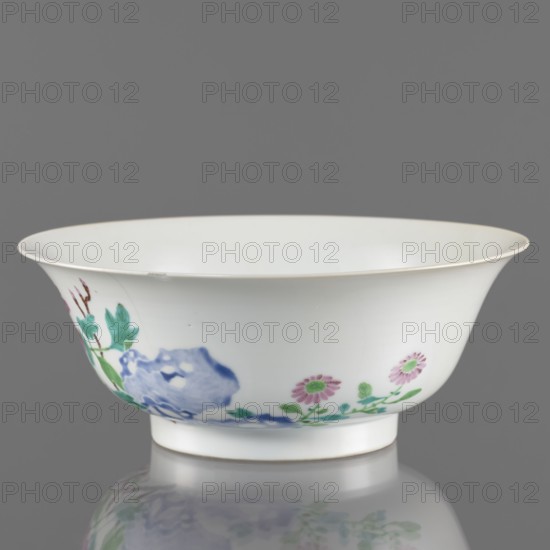 Bowl, Chinese; Qing dynasty, Yongzheng period 1723–1735. Porcelain semicircular body widening toward the upper edge; white, transparent, fritted glaze. Decoration painted with overglaze enamel paints depicting peonies, rocks and floral motifs. Vessel, height 7.6 cm, diameter 19.5 cm, weight 0.3 kg., A white porcelain bowl with a flared rim sits against a gray background, decorated with painted floral motifs including pink flowers with green centers and leaves, green foliage, and a blue rock-like form, with a glossy surface that reflects faintly below; visible colors include white, gray, pink, green, blue, and hints of brown.