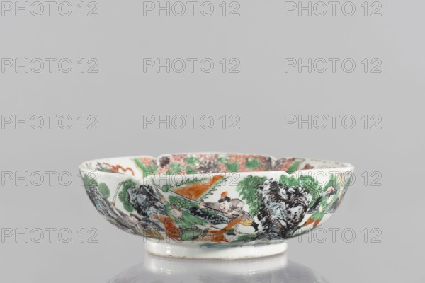 Bowl, porcelain body with white transparent glaze; decoration painted with overglaze enamel paints and iron red depicting figural and knightly scenes; colored porcelain with backdated signatures; six-lobed, bulbous belly form; 19th century, China; height 6.5 cm, diameter 20 cm., A shallow porcelain bowl with a scalloped rim sits on a short foot, decorated around its exterior with a painted scene showing a group of figures among stylized trees and rocks; visible colors include white porcelain background with green, orange, black, gray, and touches of yellow and red used in the painted figures, foliage, and landscape elements.