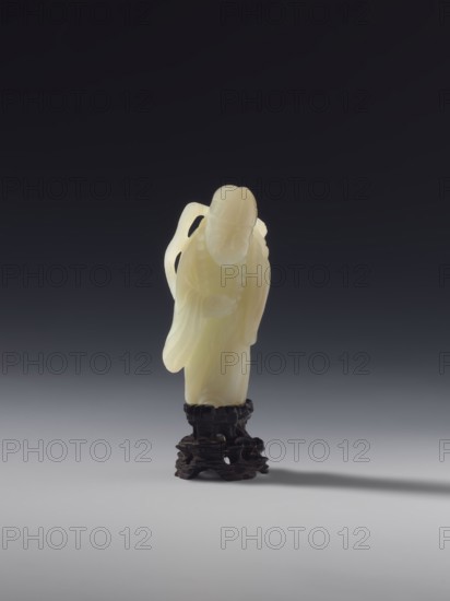 Monk with a rosary around his neck, figurine, monk subject, Chinese, Qing dynasty 1644–1911, full sculpture, 18th century, material: sculpture, height 7.8 cm, A pale yellow carved figure standing on a dark brown carved stand against a gradient background that shifts from dark gray at the top to light gray at the bottom; the figure has smooth flowing robes and a bowed head, with rounded contours and delicate carved details, and casts a soft shadow to the right on the light gray surface.