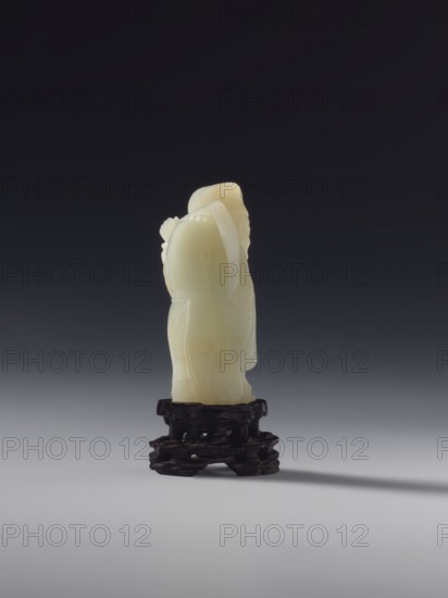 Monk with a rosary around his neck; sculptor, figurine; subject: monk; material: sculpture; culture: Chinese, Qing 1644–1911; full sculpture; 18th century; height 7.8 cm., A small carved pale yellow figure stands on a dark brown carved wooden base against a smooth gradient background that transitions from dark gray at the top to light gray at the bottom; the figure has rounded forms and draped elements suggesting clothing, with smooth and slightly translucent surfaces, and the base shows irregular organic cutouts and a textured surface.