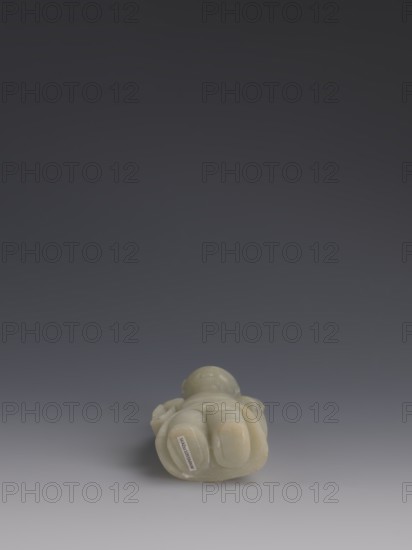 One of the Eight Immortals, Eight Immortals iconography; male figure; Chinese art; fan; Chinese culture; Qing dynasty 1644–1911, 19th century; China; sculpture; height 14.3 cm, width 5.9 cm., A small carved object rests on a smooth surface against a dark-to-light gradient background, showing a pale greenish-white stone with some areas of warm beige tones; the carving has rounded, bulbous forms and smooth polished surfaces with subtle variations in translucency, and a small rectangular lighter patch is visible on one rounded area.