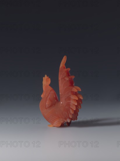 Rooster; creator, sculptor; gift; Chinese art; Chinese; Qing 1644–1911; figurine of a rooster; 18th–19th century, China; sculpture; 8.5 cm high, 7.0 cm wide, 2.6 cm deep., A carved rooster figurine in shades of orange and red with translucent areas, showing detailed feather carving and a raised tail, standing on a smooth gray surface against a dark gray background, casting a soft shadow.