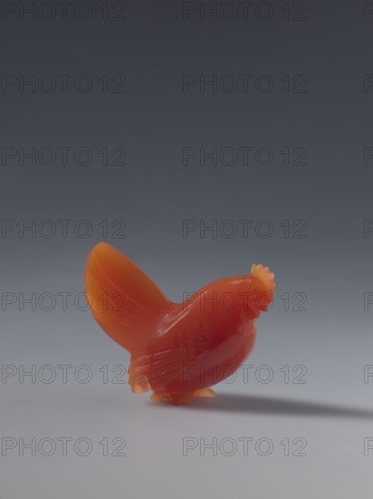 Hen, unknown creator sculptor, Chinese, Qing 1644–1911, 18th–19th century, figurine of a hen, sculpture; height 4.5 cm, width 5.0 cm, depth 2.3 cm., A small sculpted bird made of glossy orange and red material stands on a smooth light-gray surface, casting a soft shadow; the bird shows a rounded body, raised tail with layered feather details, a comb-like crest on its head, and subtle carved wing and leg features against a gradient background that shifts from dark gray at the top to medium gray near the horizon.