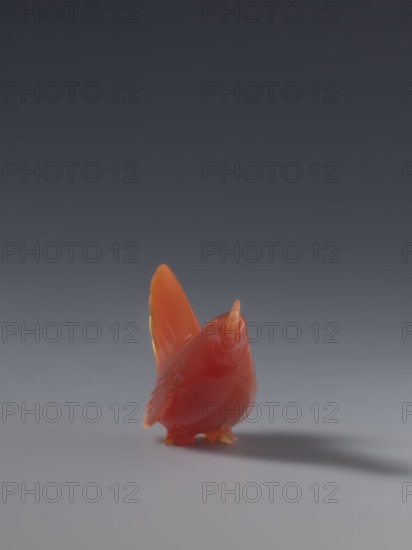 Hen; unknown sculptor; Chinese, Qing dynasty 1644–1911; 18th–19th century; sculpture figurine of a hen; material: Chinese art; dimensions: height 4.5 cm, width 5.0 cm, depth 2.3 cm., A small glossy bird figurine in shades of red and orange stands on a smooth surface, with a slightly darker red body and brighter orange on its wings and beak, casting a soft shadow; the background transitions from a dark gray at the top to a lighter gray near the surface.