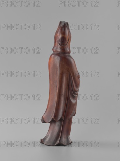 Guanyin Bodhisattva, unknown sculptor, figurine, Chinese art, Chinese culture, goddess, Chinese Buddhism, Qing 1644–1911, bodhisattva iconography, wood carving, solid polished, 19th century, China, sculpture, height 32 cm, A carved wooden figure standing upright on a flat surface, shown from a rear three-quarter view; the figure is draped in flowing robes with visible carved folds and a hood covering the head. The wood has a smooth, polished surface with warm brown and reddish-brown tones and subtle darker brown areas in the recesses and along the base. The background and surface are neutral gray, providing contrast with the brown and reddish hues of the figure.