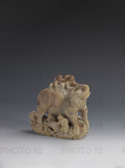 Buffalo with calves and shepherds, purchase, Buffaloes; Chinese art; figurines; Chinese culture; Qing dynasty 1644–1911. Sculpture made of decorative Fushan Mountains Zhejiang Province soapstone, full figure, natural patina. 18th–19th century, China. Height: 16.5 cm., A carved stone sculpture in beige and light brown tones depicts a large animal resembling an ox with curved horns standing on a decorative base, with a group of small human figures clustered around and atop the animal; the figures and the animal share the same stone color with subtle variations of darker brown and pale yellow, and the sculpture sits against a smooth gradient background shifting from dark gray at the top to pale gray at the bottom.