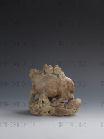 Buffalo with calves and shepherds, unknown sculptor; purchase provenance; buffaloes; Chinese art; figurines; Chinese culture; Qing dynasty 1644–1911; sculpture made of decorative Fushan Mountains Zhejiang Province soapstone; natural patina; 18th–19th century; China; sculpture; height 16.5 cm, A carved stone sculpture depicting the rear and side view of an animal resembling an ox or buffalo standing on an ornate base with swirling forms and additional smaller carved shapes; the stone shows mottled tones of brown, tan, beige, and hints of green with smoother and slightly weathered surfaces, set against a gradient background that transitions from dark gray at the top to lighter gray near the bottom.